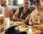a shirtless Randy from Trailer Park boys and his media team sit down at a restaurant booth to enjoy a taco burger. Randy has a cowboy hat and sunglasses on