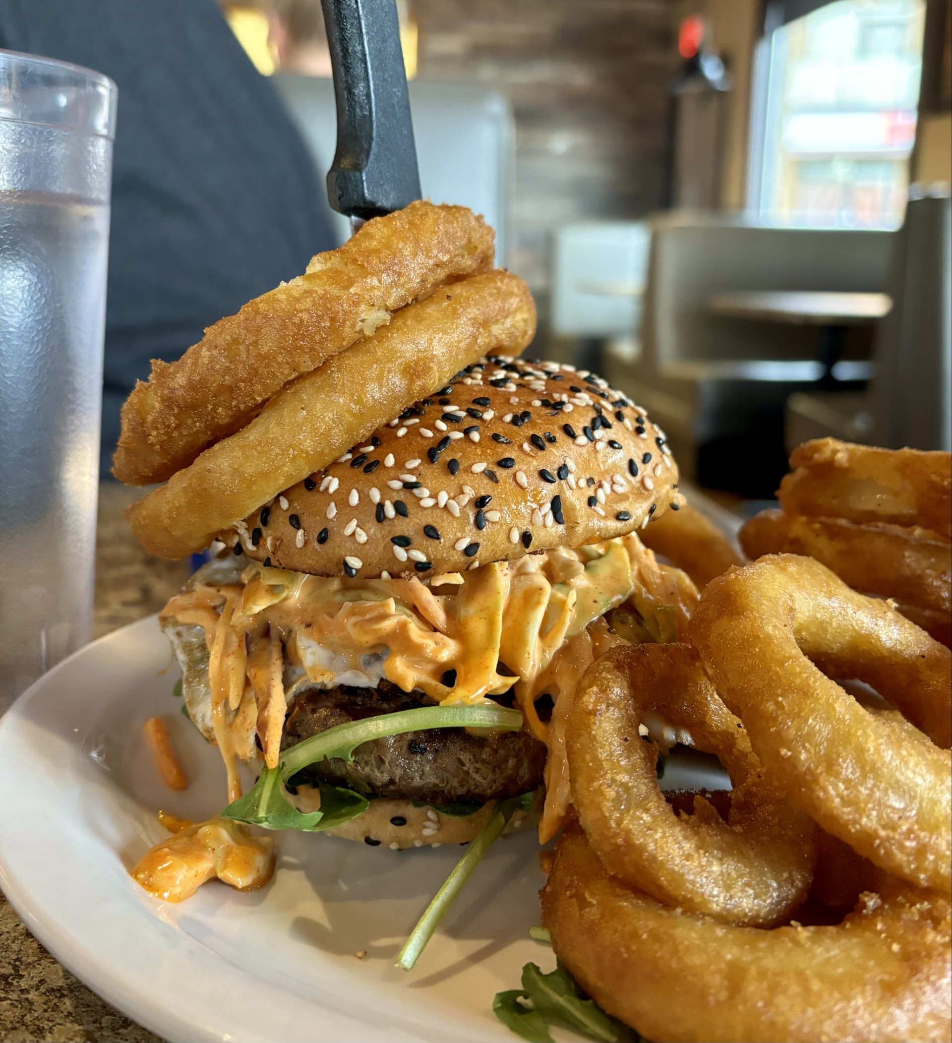 A burger with a house recipe Canadian beef patty that is topped with tender, braised Korean beef short rib. Layered with zesty gochujang coleslaw, peppery arugula, pickled carrots, and a perfectly fried dark yolk egg. Finished with crispy onion rings on top.