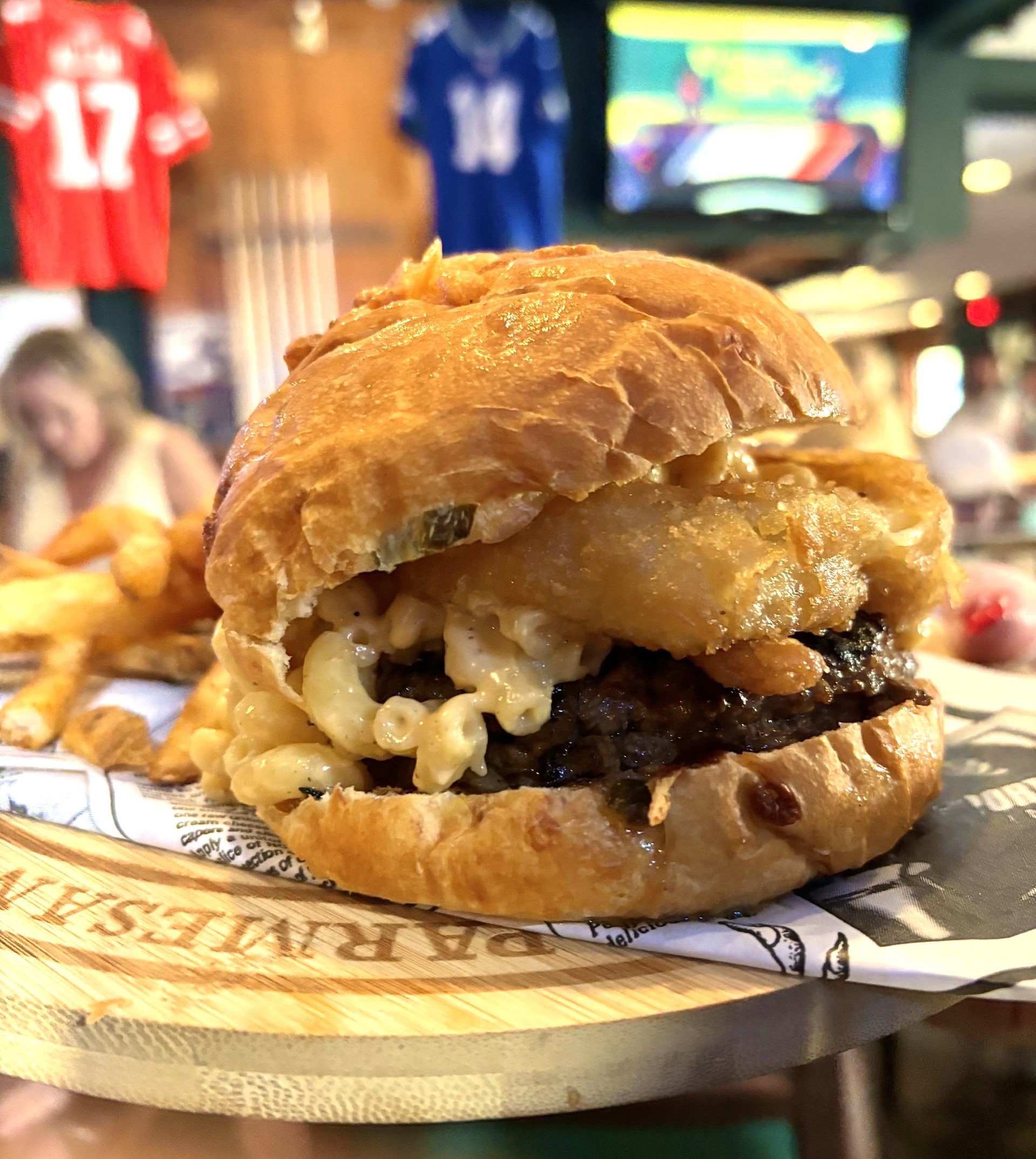 A beef burger with melted cheese and mac & cheese oozing out the sides.