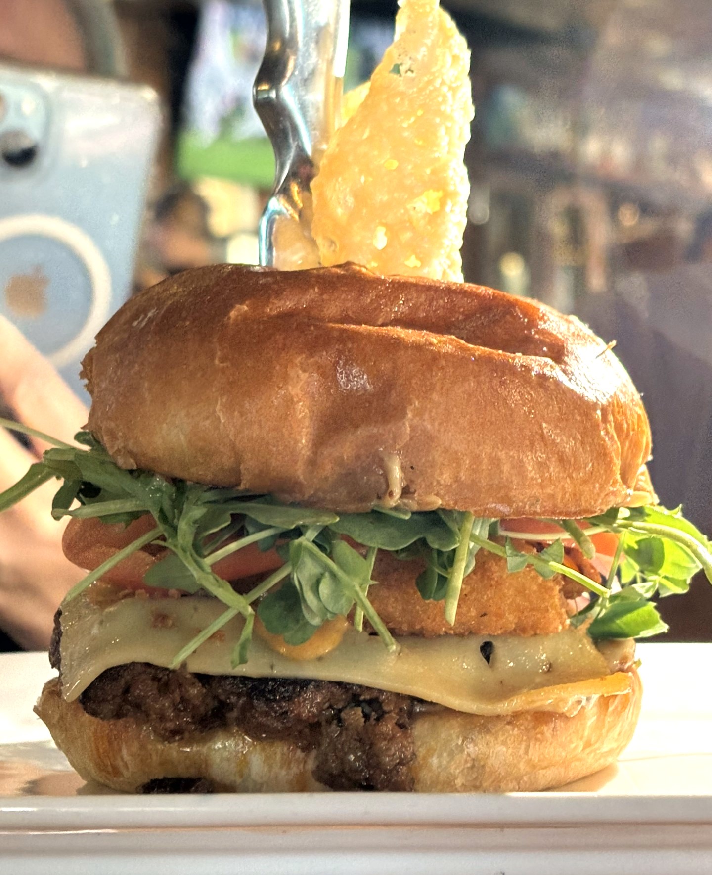 a beef burger with mozza cheese, arugula, tomato, on a bun with a crispy parmesan crisp stuck onto the top of the bun.